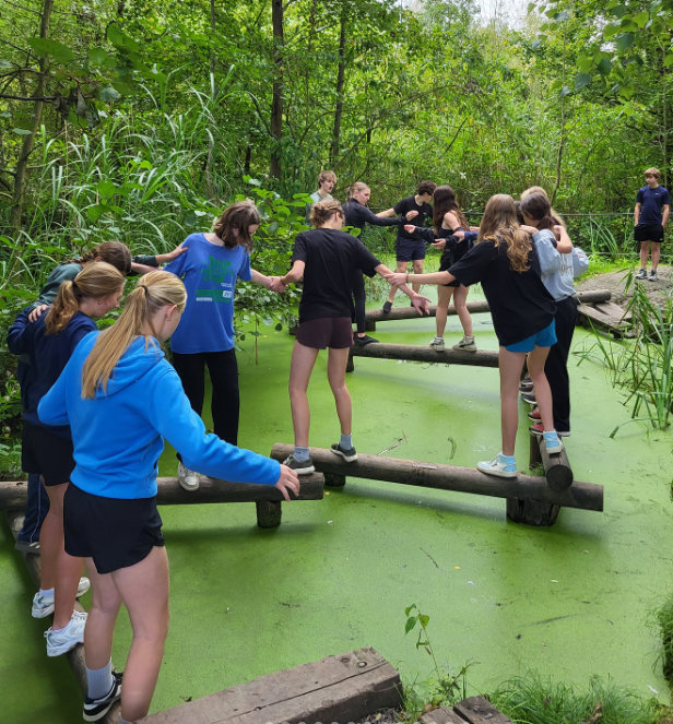 Leerlingen lopen op houten balken boven een plas water